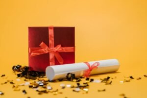 A festive red gift box and diploma amidst confetti on a vibrant yellow background.