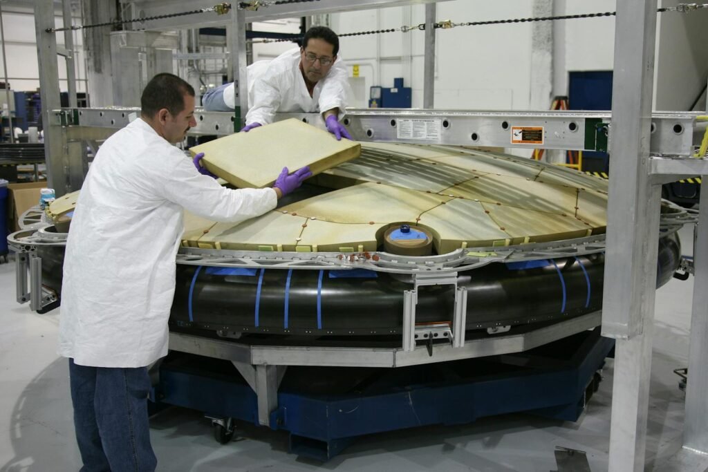 Technicians work diligently to assemble a spacecraft part in a modern industrial facility.