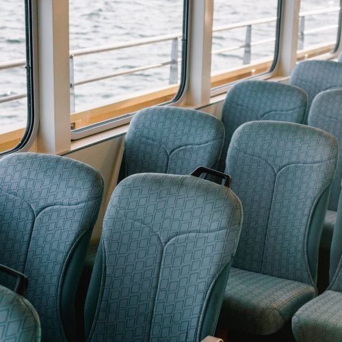 A serene view of unoccupied blue seats inside a boat with windows showing the sea.