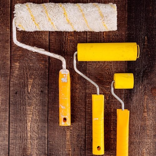 Top view of yellow paint rollers arranged on a wooden table for DIY projects.